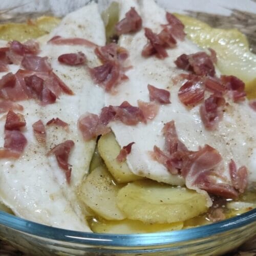 Lubina en el horno con patatas, cebolla, pasas y jamón.