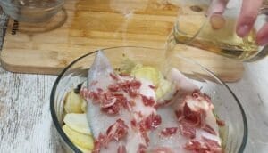 Lubina pescado en el horno con patatas, cebolla, pasas y jamón.